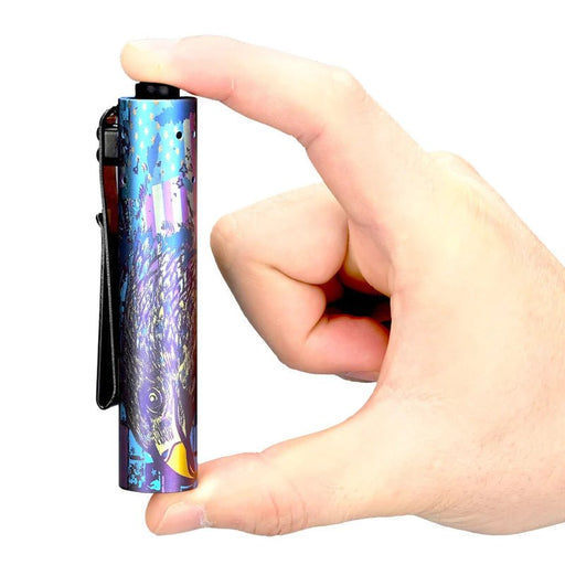 A hand holding a small Acebeam Rider RX 2.0 ANODIZED Titanium (Limited Edition) flashlight with a colorful bird design on it between the thumb and index finger.