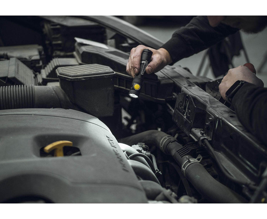 A person uses the Armytek Partner C2 Magnet USB - Warm flashlight to inspect an engine in a car workshop.