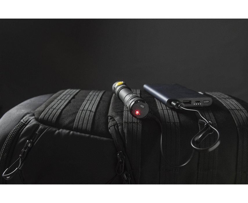 An Armytek Partner C2 Magnet USB - Warm flashlight in black with red light, plus a portable charger, rest on a black backpack against a dark background.