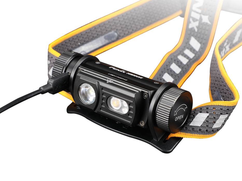 The Fenix HM60R is an outdoor headlamp in black and orange, equipped with a strap and two LED lights capable of delivering up to 1300 lumens. An additional cable connects to the side, enhancing its functionality.