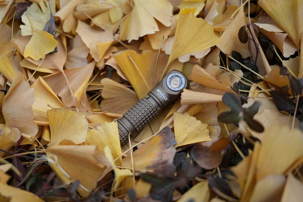 The Manker E03H III flashlight rests among a bed of dried yellow and brown leaves.