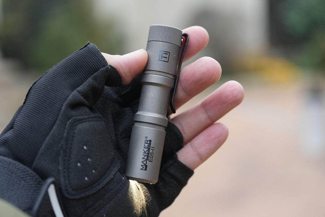 A hand in a black glove holds the Manker E05 II - Stonewashed Ti, a compact titanium flashlight ideal for everyday carry.