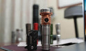 Several Manker flashlights, including the Manker MC13 II Pocket EDC Flashlight - Titanium & Copper, are displayed on a desk with additional flashlights blurred in the background.