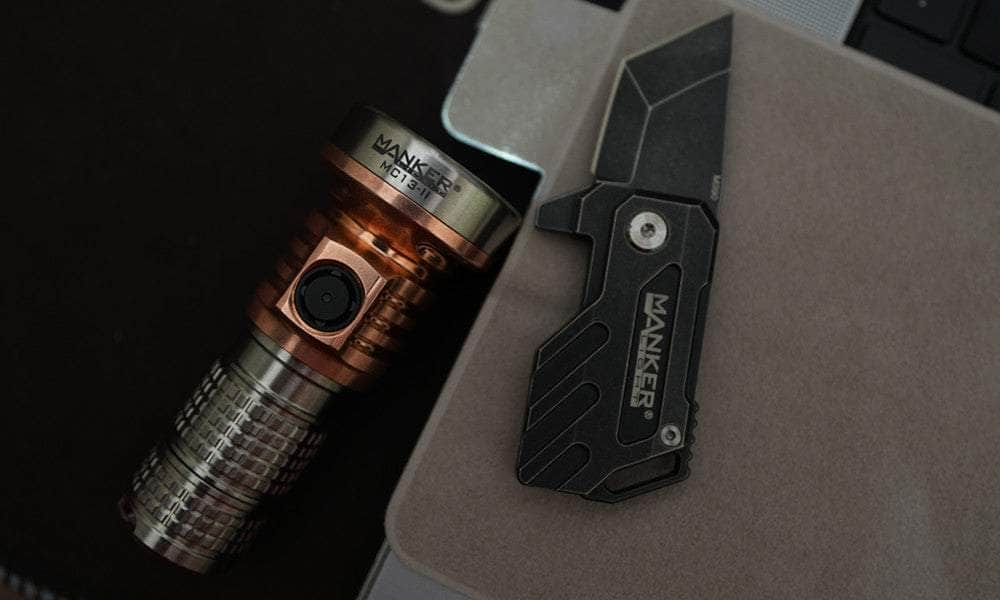 A compact Manker MC13 II Pocket EDC Flashlight - Titanium & Copper and a foldable knife, both marked with the brand "Manker," are placed on a light brown surface next to a silver and black electronic device.