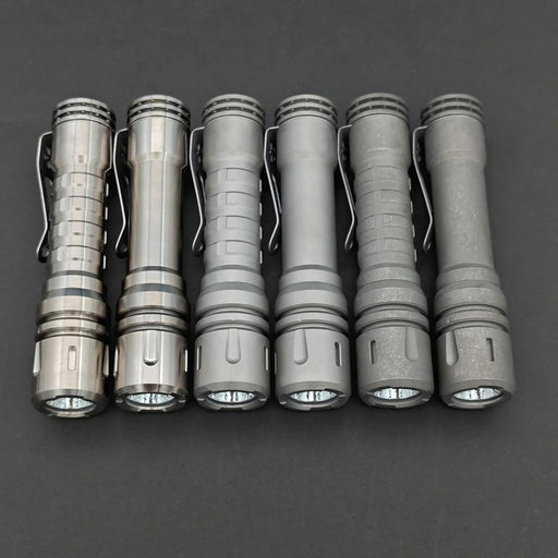 Six ReyLight LANapple - Ti metallic flashlights, each powered by a rechargeable 14500 battery, are placed in a row on a dark background.