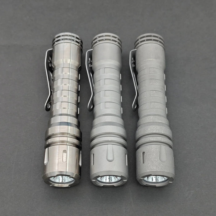 Three ReyLight LANapple - Ti cylindrical flashlights, with metallic exteriors featuring clips, are powered by rechargeable 14500 batteries and arranged vertically on a dark background.