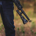 Close-up of a person holding a black rifle with the Weltool F11R attached, featuring a rechargeable long-range LED flashlight and laser sight outdoors, while wearing blue jeans.