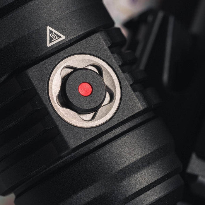 Close-up of the Weltool F11R, featuring a black, ridged component with a small red button in the center, surrounded by a metal ring. A triangular caution symbol is visible on the top left of the USB-C charging structure.