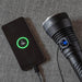 A 73%-charged smartphone is connected to the Weltool F6R high-lumen flashlight on a gray fabric surface, ready to unleash its Turbo Output 5.