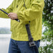 A person in a green jacket holding a fishing rod with a high-lumen Weltool F6R flashlight hanging from their jacket, standing near a body of water.