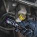 A gloved hand holds the Weltool M4-365 UV flashlight near a car engine, illuminating components with its 365nm beam.