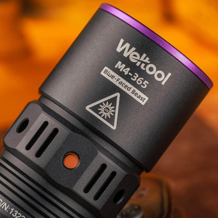 Close-up of the Weltool M4-365 UV flashlight in black, emitting at 365nm. It features a triangular warning symbol, indicating its high radiation flux capabilities.