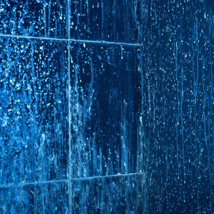 Close-up of dark blue tiled walls sparkling under the Weltool M4-365 UV flashlight, accentuating water droplets and streaks.