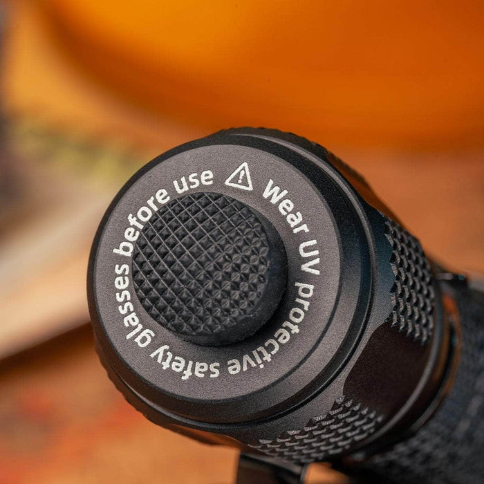 Close-up of the Weltool M4-365 UV flashlight button with a textured grip. Text reads: "Wear UV protective safety glasses before use due to high radiation flux.