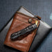 A Weltool T1 Pro V2 black, compact flashlight rests on a brown leather wallet, which is placed on a closed book with a textured dark cover.