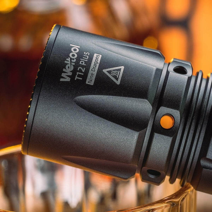 Close-up of the Weltool T12 Plus Nine Dragons tactical flashlight head, highlighting its intricate engravings and robust design, powered by a 21700 battery, with a blurred warm-toned background.