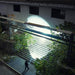 Using a Weltool T12 Plus tactical flashlight, a person illuminates a staircase outside an old building at night, highlighting the overgrown foliage.