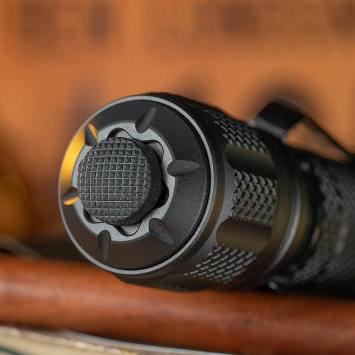 Close-up of the Weltool T12 Plus, showcasing its black textured flashlight button with a knurled grip, crafted for tactical use and set against a blurred background. The rugged design suggests its 3TAC function and compatibility with a powerful 21700 battery.