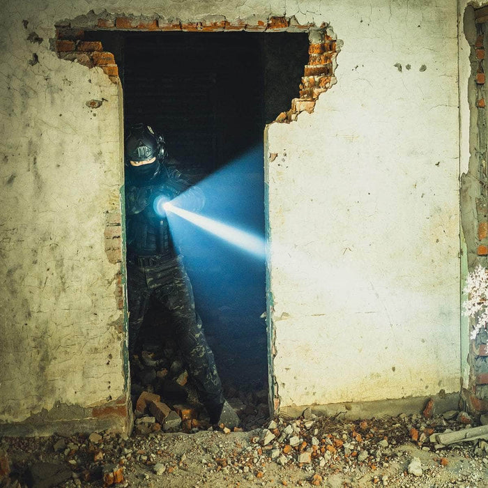 A person in tactical gear stands in a partially destroyed doorway, illuminating a dim room littered with debris using the Weltool T12 Plus tactical flashlight, which is powered by a 21700 battery.