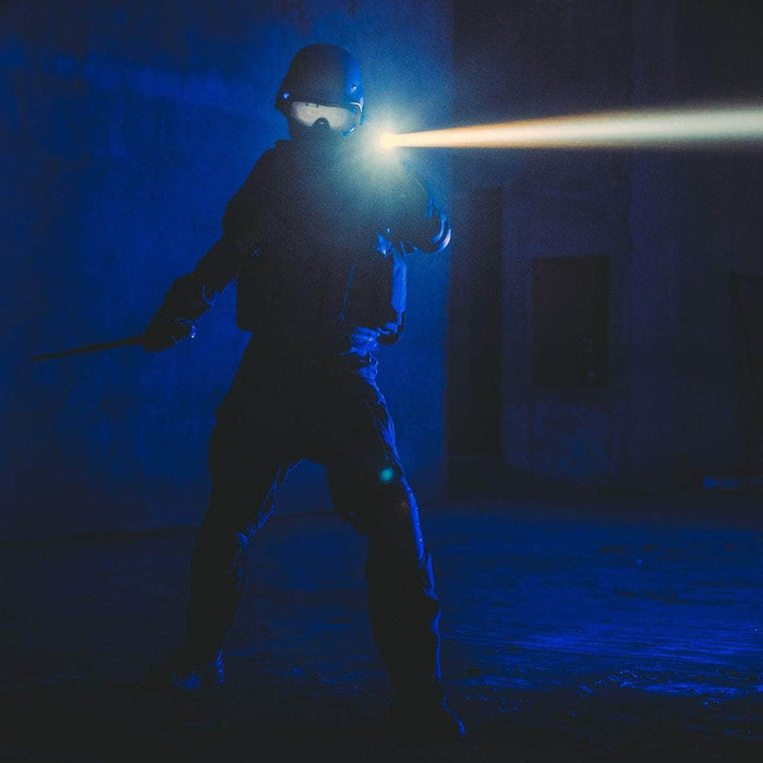 Dressed in tactical gear, a person stands in a dark room holding a baton and the Weltool W3Pro TAC Mini flashlight, its LEP light source cutting through the darkness.