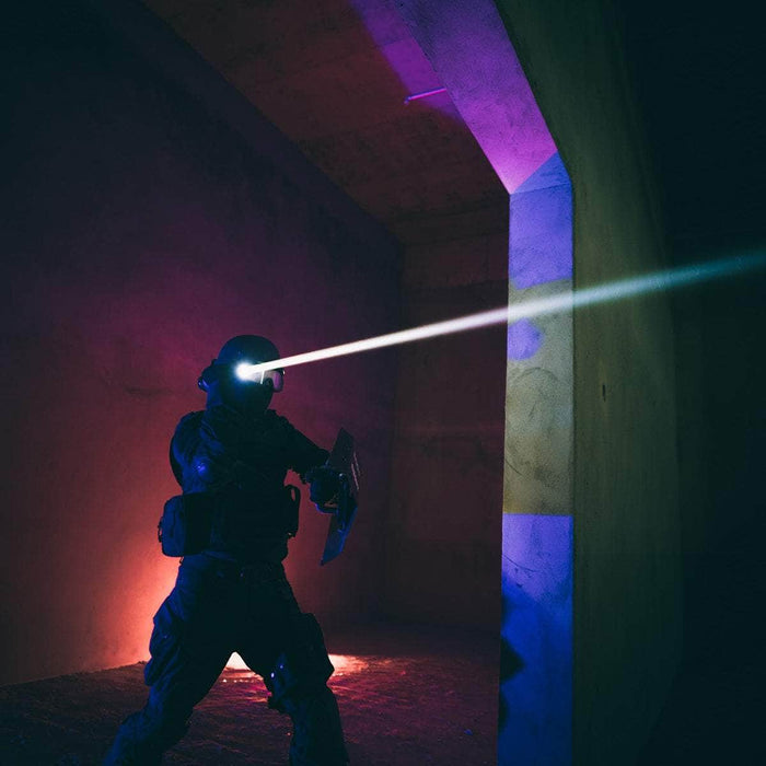 In a dimly lit concrete room, a person in tactical gear with a helmet emits a bright beam of light from the Weltool W3Pro TAC Mini's robust LEP source, ensuring visibility using its reliable rechargeable lithium-ion battery.